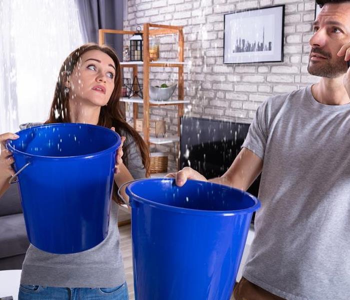 A man and woman catching water in blue buckets. 