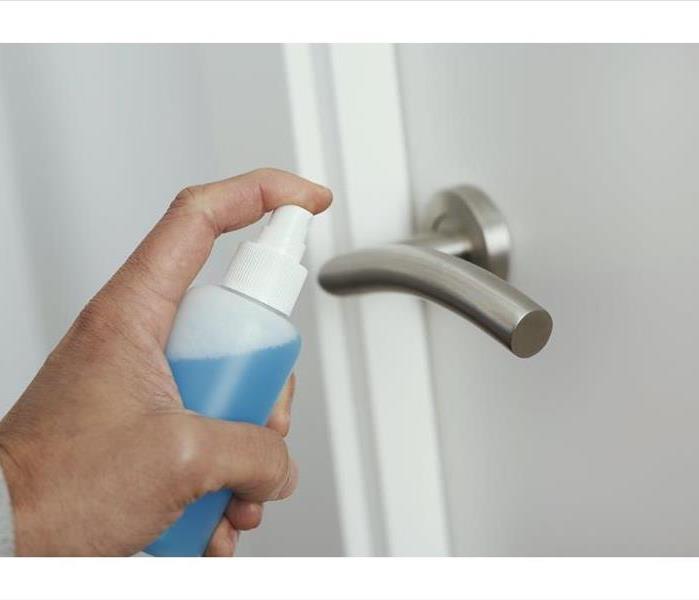 hand spraying a blue liquid onto a silver door handle