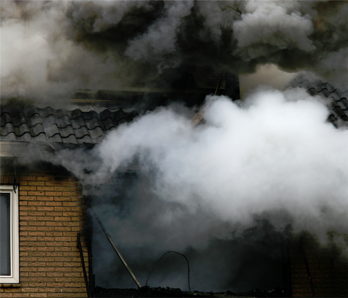a fire damaged house with smoke billowing from the windows
