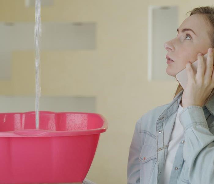 A woman on the phone catching water in a pink bucket